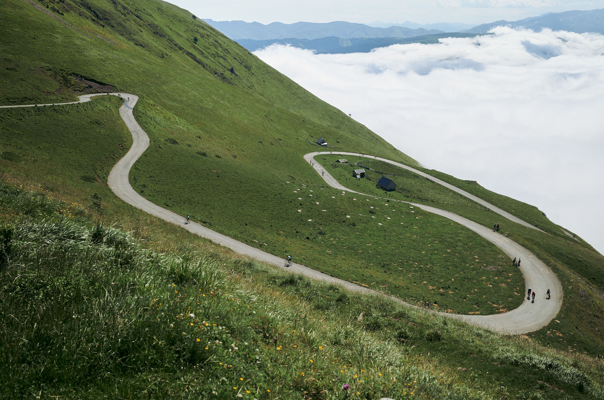 POC helm, bril & protectoren - veiligheid & style voor MTB & road POC merkbeeld met fietsers op een afgelegen bergpasweg in een alpine omgeving boven de wolken.