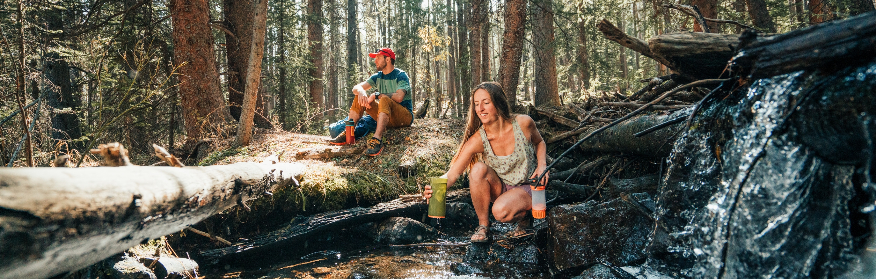 Eine Frau und ein Mann trinken gefiltertes Wasser aus einer Waldquelle