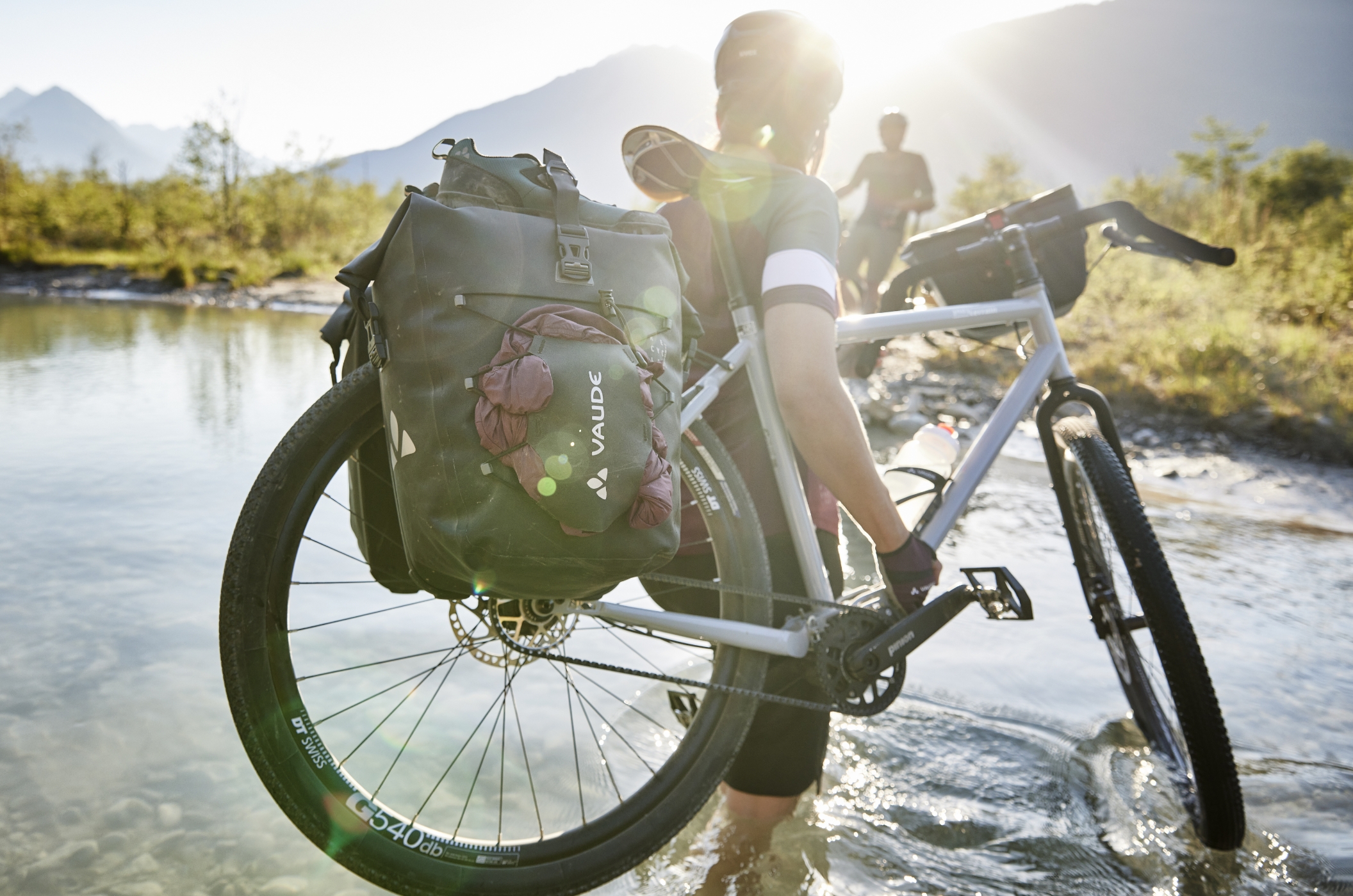 VAUDE „ReCycle“ Bike Bags Bikepacker carrying their bicycle with VAUDE panniers through a mountain stream in the sunlight.