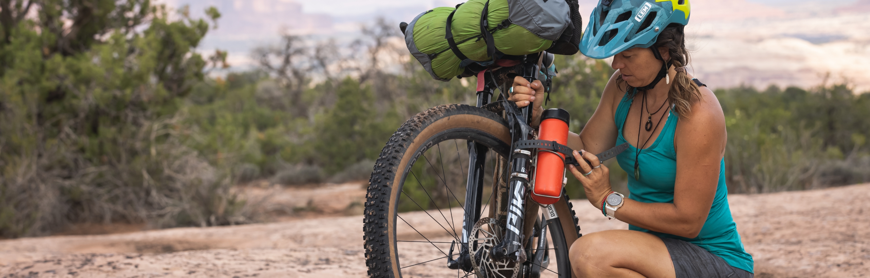 Chica colocando en bidón de agua en una bicicleta bikepacking en el campo