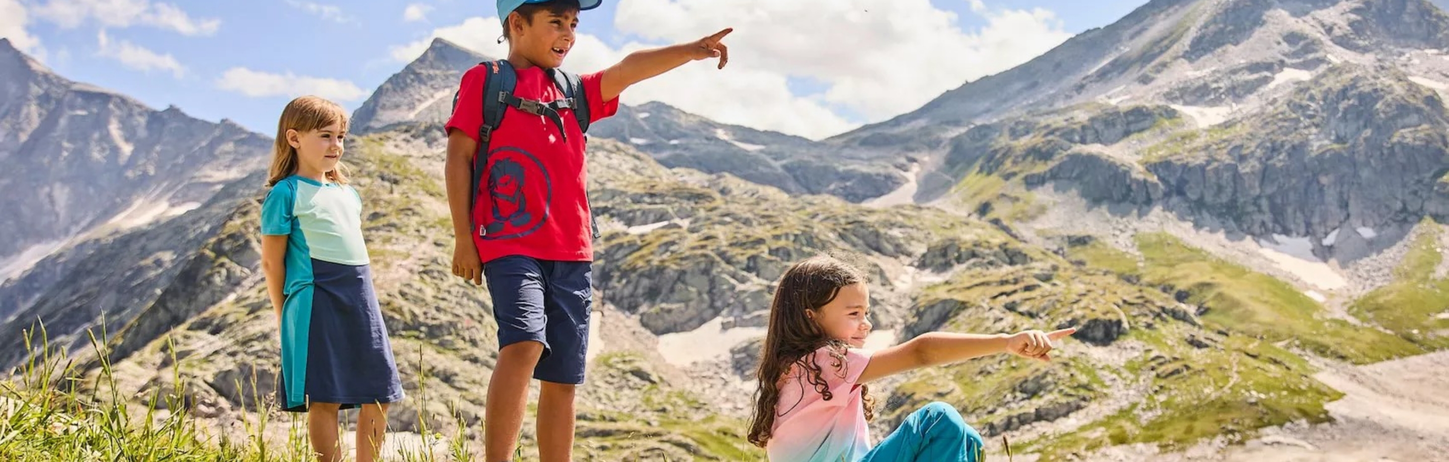 Drie kinderen in Trollkids outdoor kleding ontdekken de bergen en genieten van een avontuur in de natuur.
