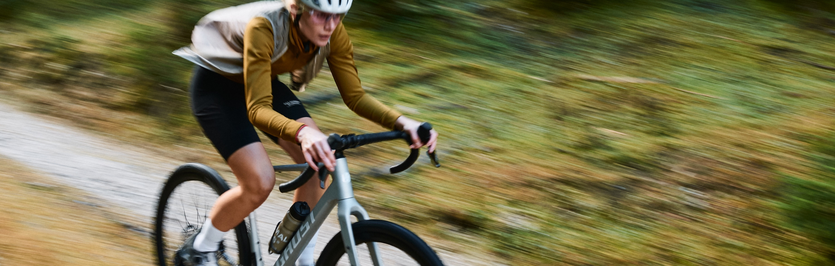 Action-Aufnahme einer Ghost Bikes-Fahrerin im gelben Trikot, die konzentriert auf einem Schotterweg bergab fährt.