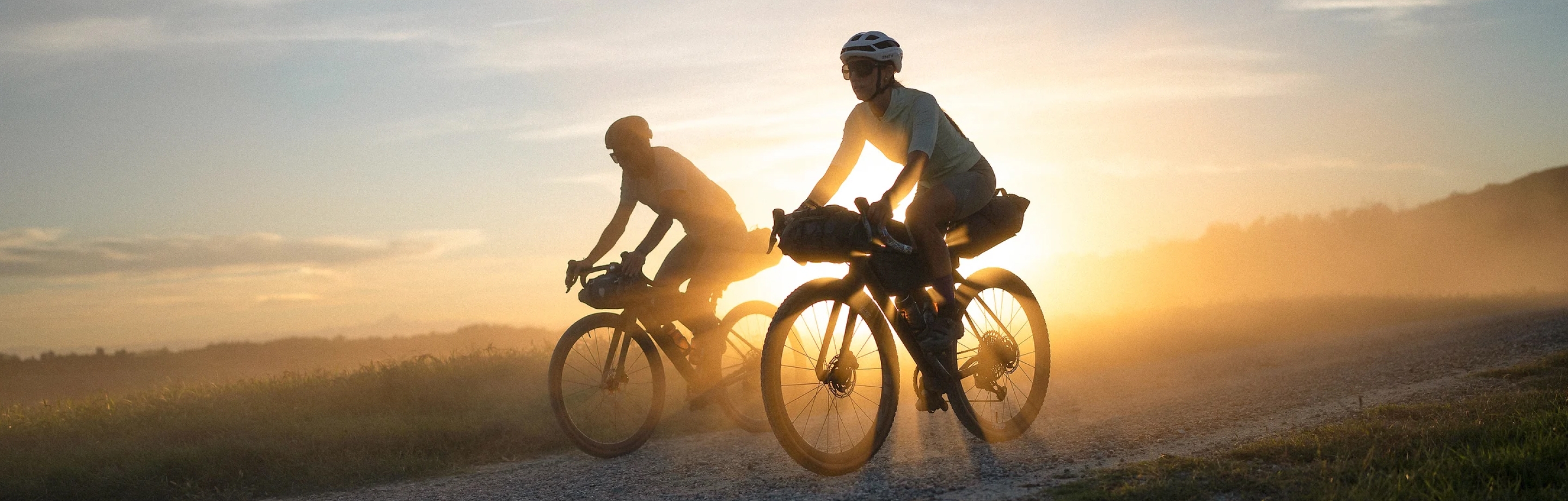 Twee fietsers rijden bij zonsondergang in Odlo outdoor-kleding over een grindpad.