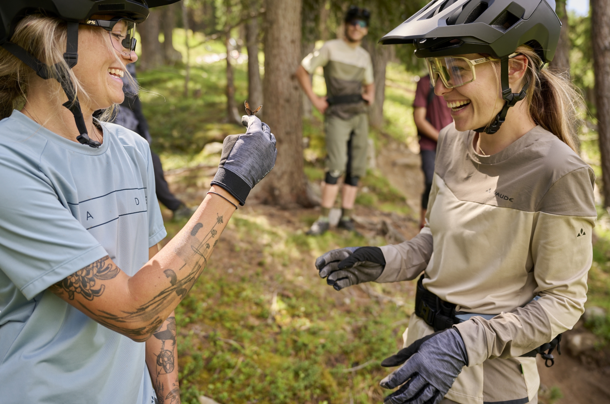 VAUDE – The Spirit of Mountain Sports Two mountain bikers in VAUDE bike apparel smiling at a butterfly in the forest.