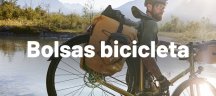 Persona con lleva una bicicleta con bolsas amarillas de bici y esta cruzando un río tranquilo en un día soleado