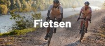 VAUDE - functionele producten voor fietsers Een man en een vrouw in VAUDE-fietskleding rijden op gravelbikes langs een rivier.