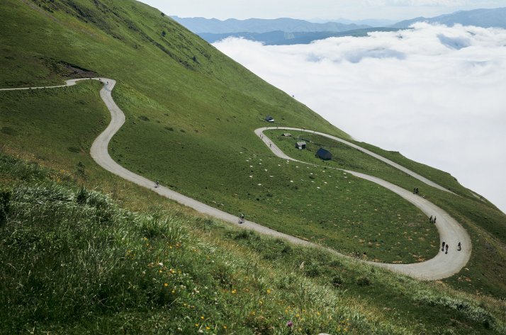 POC – Helme, Bekleidung und Accessoires für MTB & Road POC Markenbild mit Radfahrern auf einer abgelegenen Passstraße in alpiner Kulisse über den Wolken.