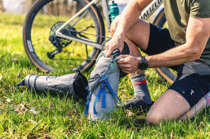 Ein Bikepacker, der vorsichtig einen Schlafsack in seine Satteltasche packt.