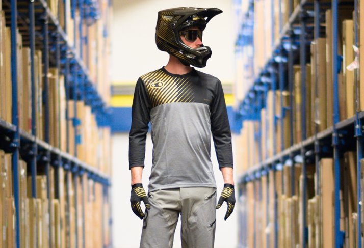 A rider in downhill clothing stands in a shelf aisle.