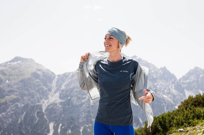 A hiker in VAUDE apparel smiling at the top of a mountain..