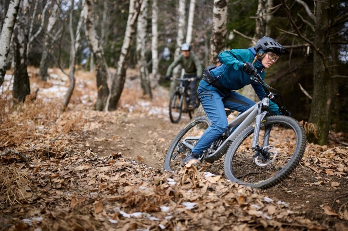 VAUDE cycling apparel – functional gear for every ride Mountain biker in a VAUDE jacket and trousers leans into a bend on a leaf-covered trail