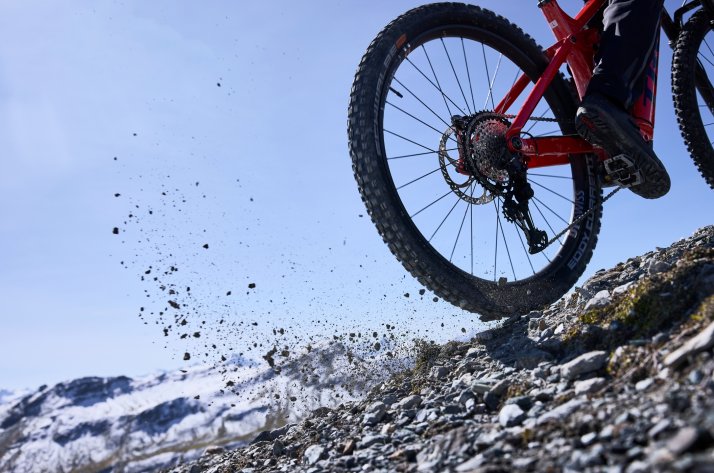 Osoba wjeżdża pod górę na kołach DT Swiss Hybrid, wzniecając żwir.