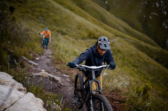 Protections et vêtements VTT Leatt : protection de la tête aux pieds Deux vététistes vêtus de vestes Leatt poussent leurs vélos pour gravir une pente verdoyante