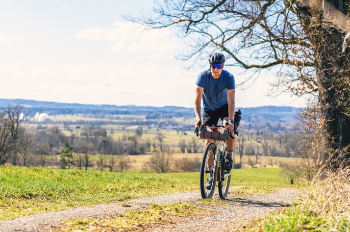  Ein engagierter Bikepacker fährt mit einem voll beladenen Gravel-Bike auf einem Waldweg und präsentiert dabei essenzielle, leichte Ausrüstung für mehrtägige Radtouren.