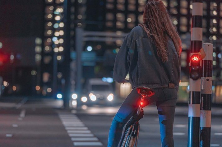 Luces para bicicleta: chica sobre una bicicleta de noche en la ciudad Mujer en bicicleta esperando en un semáforo en rojo de noche, con luz trasera AXA encendida, en una calle urbana.