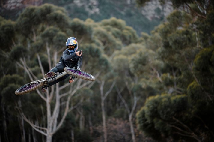 Vêtements VTT Leatt : une combinaison parfaite de style et de fonctionnalité Un vététiste en tenue Leatt saute, son vélo tendu devant lui, devant un décor forestier