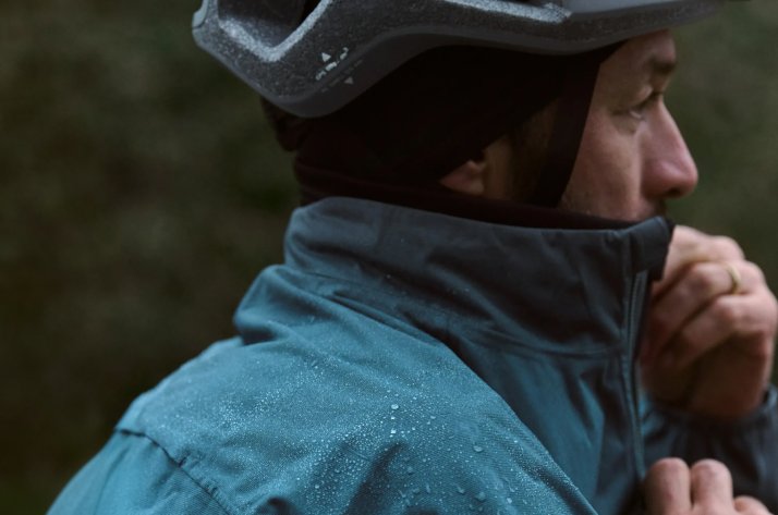 CRAFT Radfahrer zieht den Kragen seiner Craft Regenjacke hoch, auf dem Stoff perlen Wassertropfen ab