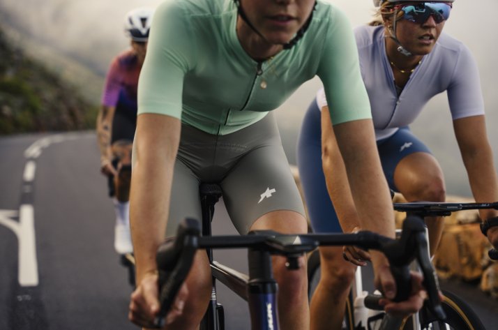 Scène dynamique de cyclistes en tenue ASSOS sur une route sinueuse de montagne.