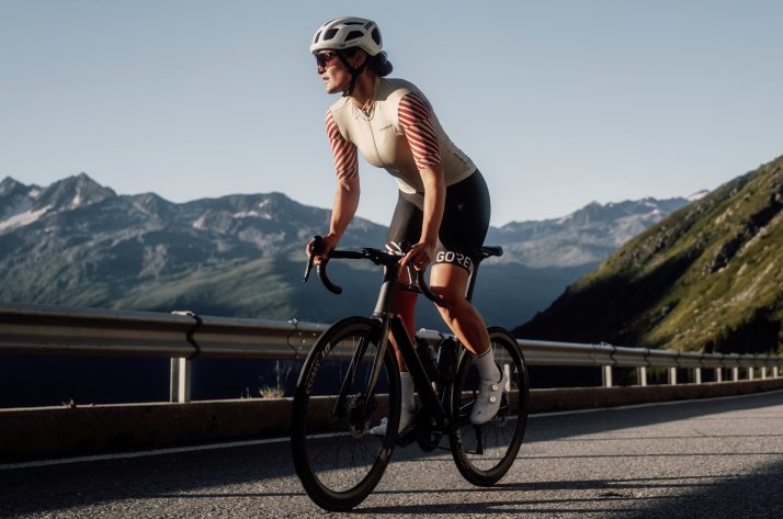 Découvrez la collection GOREWEAR Swiftride Optical pour le vélo de route et le Gravel. Une femme roule à vélo sur une route panoramique dans les Alpes.