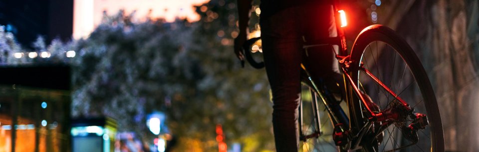 Persona parada con su bicicleta con su luz trasera Ravemen encendida en el atardecer. 