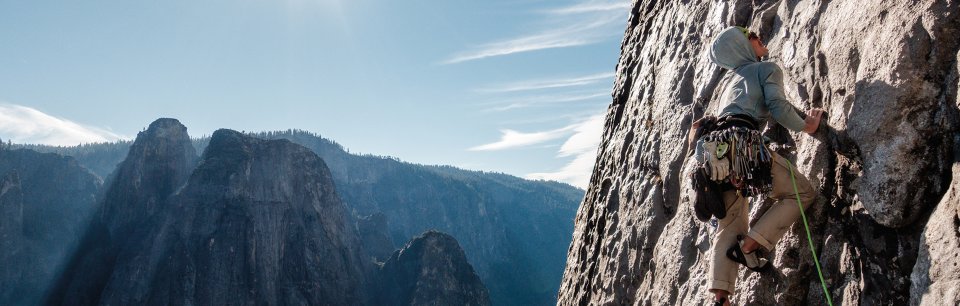 Persona escalando una montaña vertical en un día despejado