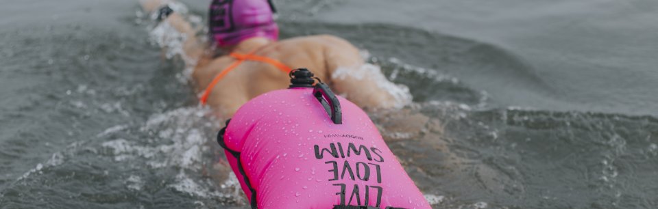 Une nageuse utilise la bouée rose BUDDYSWIM pour plus de sécurité et de visibilité en nageant en eau libre.