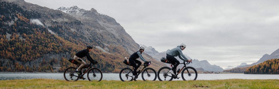 Tres ciclistas con bicicletas bikepacking pedaleando cerca de un lago en un dia nublado