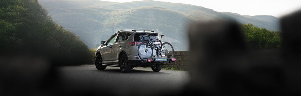 Coche con un portabicicletas en el maletero, donde lleva una bici. Está aparcado en una zona verde