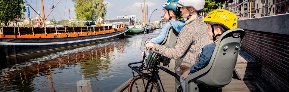Une mère roule avec ses deux enfants dans des sièges de vélo Polisport.