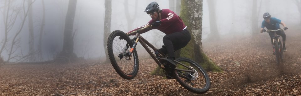 Un vététiste vêtu d'un maillot 100 % rouge foncé traverse à vélo une forêt automnale brumeuse