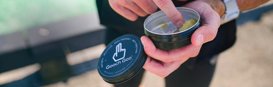 Jemand nimmt mit dem Finger Gooch Goo Balsam aus einer geöffneten Dose und hält den Deckel mit Logo in der anderen Hand