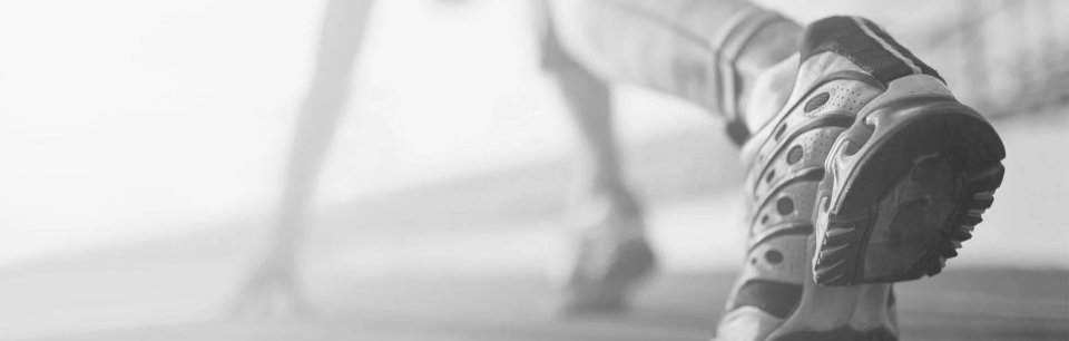 Persona en posición de salida para correr con unas zapatillas y manos apoyadas en el suelo e imagen en blanco y negro