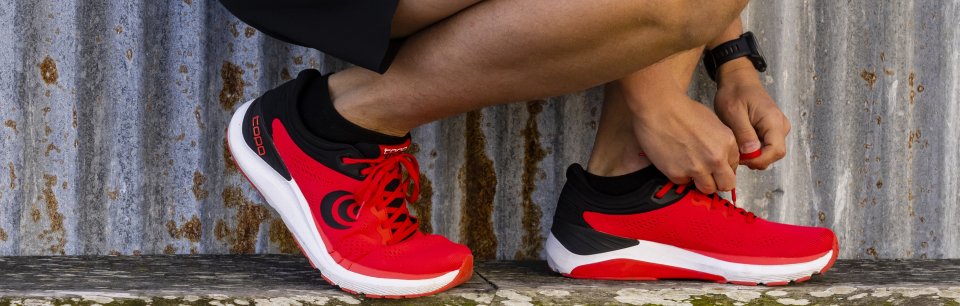 Imagen de pies con zapatillas rojas, negras y blancas de la marca Topo Athletic