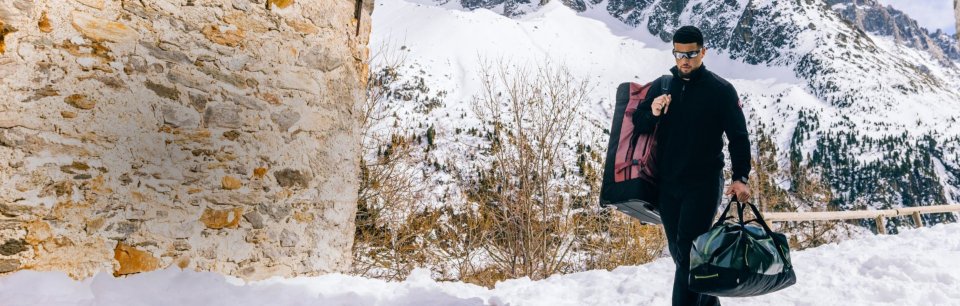 Hombre caminando por un sendero con nieve cargando dos bolsos Eagle Creek.