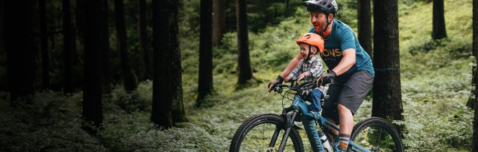 Hombre con su hijo en una bicicleta con una silla para bebés en el bosque