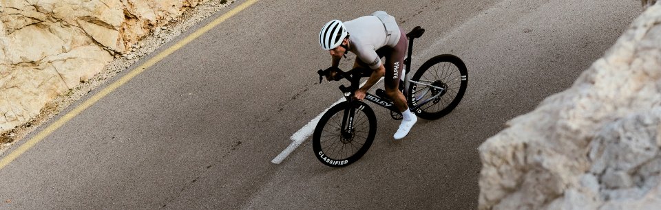 Ein Rennradfahrer in Rapha Fahrradbekleidung fährt mit hoher Geschwindigkeit auf einer Bergstraße und zeigt aerodynamische Performance.