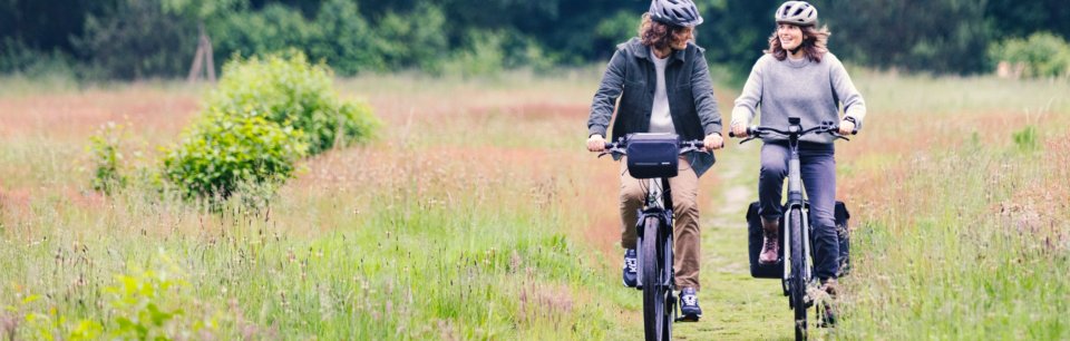 Zwei Radfahrer mit Basil Fahrradtaschen und -körben genießen eine entspannte Tour durch die Natur.