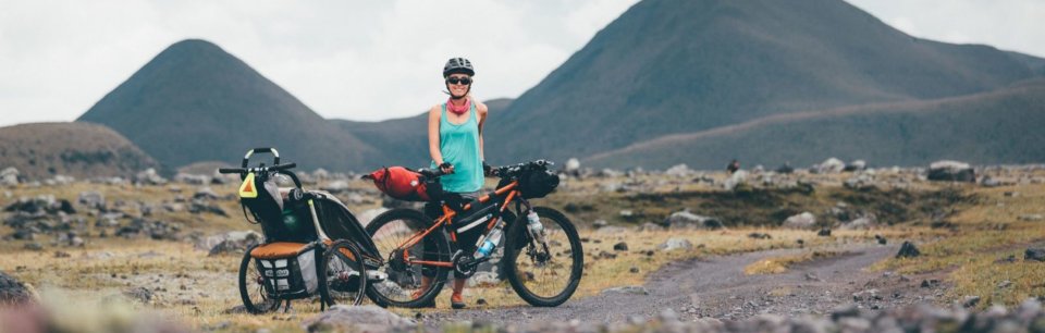 Mujer en n lugar con aspecto volcánico con una bicicleta bikepacking y con un remolque