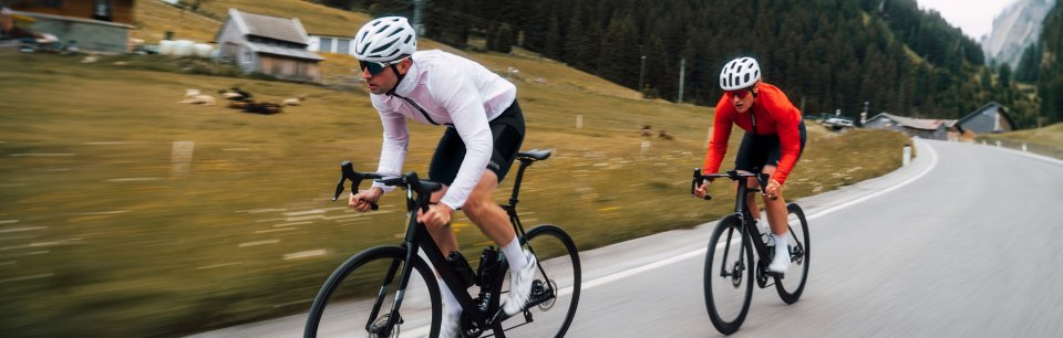 Un ciclista e una ciclista in bici su strada sfaltata con abbigliamento GOREWEAR