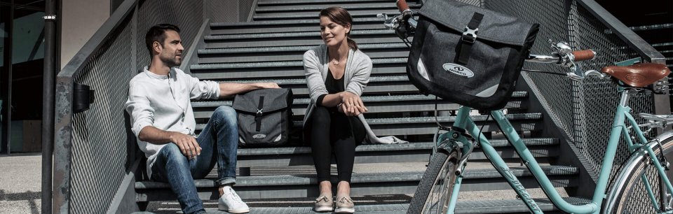 Zwei Personen sitzen auf einer Treppe mit Norco Fahrradtaschen und Citybike – perfekt für urbanes Pendeln.