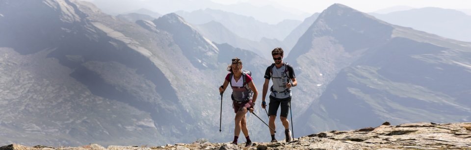 Zwei Sporttreibende mit Karpos Kleidung steigen mit Tourenski durch alpines Gelände.