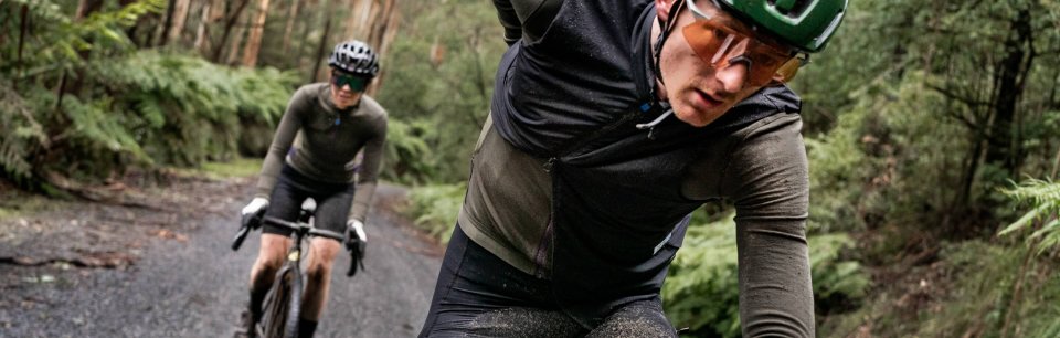 Un ciclista gravel con l'abbigliamento MAAP pedala davanti a un altro attraverso il bosco.