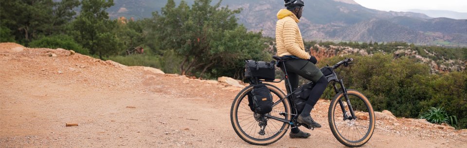 Radfahrer mit Restrap Gepäcktaschen am Gravelbike blickt auf einem Schotterweg über eine Berglandschaft