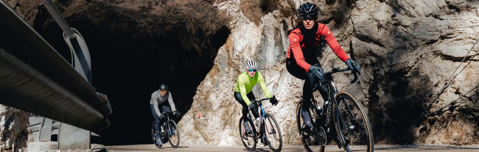 Een groep fietsers in Castelli-jassen rijdt een rotsen tunnel uit