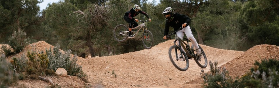 Zwei Mountainbiker mit Sixpack Racing Komponenten bei einem Sprung auf einer Offroad-Strecke im Wald.