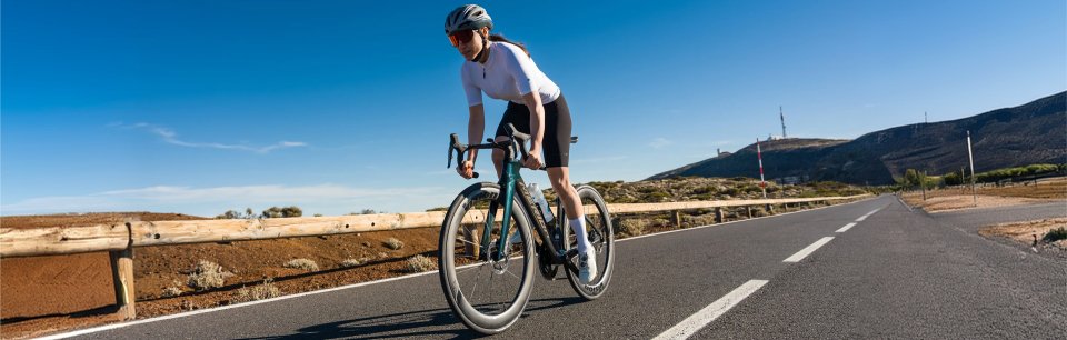 Rennradfahrerin fährt auf ihrem MERIDA Rennrad eine sonnige Straße durch karge Berglandschaft
