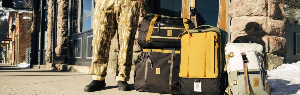 Mochilas de la marca Topo Designs en la entrada de un edificio con fachada de piedra.