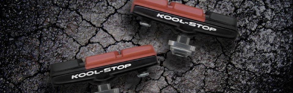 Zwei Kool-Stop Bremsbeläge in Schwarz und Rot, präsentiert vor einem strukturierten, rissigen Hintergrund.