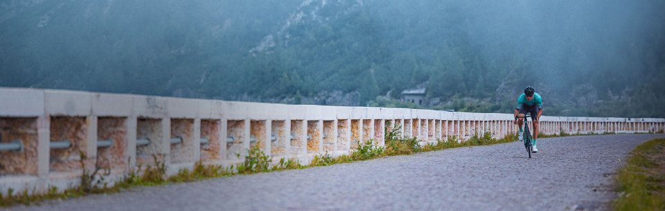 Ein Rennradfahrer auf einem Bianchi Bike fährt mit hoher Geschwindigkeit über eine Bergstraße und verkörpert sportliche Performance.
