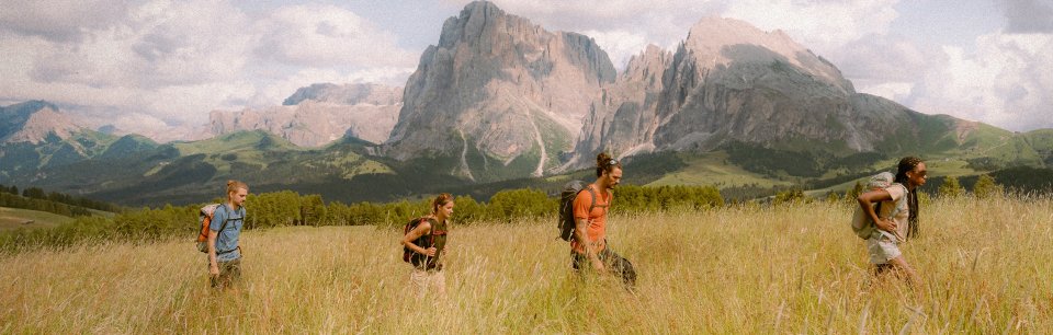 Personas caminando por un campo con ropa de montaña Salewa y con montañas de fondo